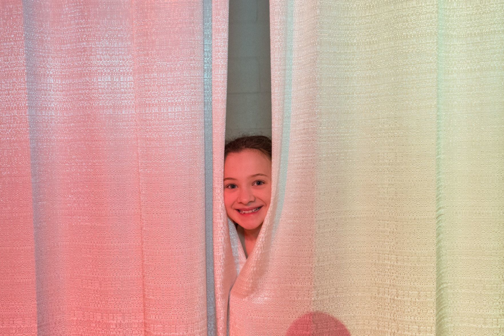 Liliana Deweese (8) pokes her head out from the cutrains backstage